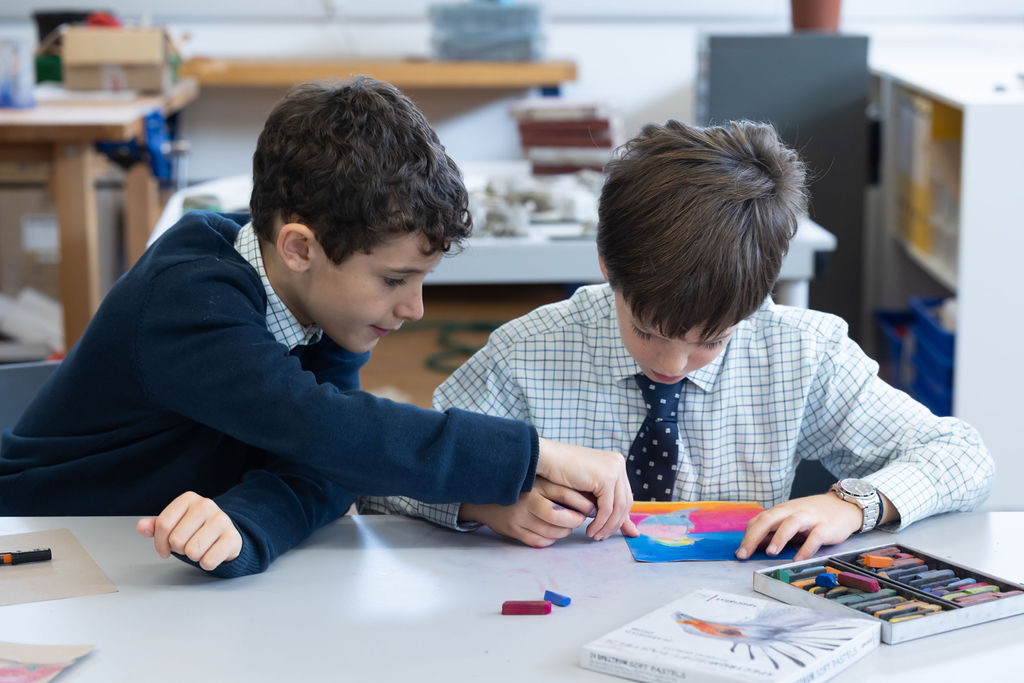 Two boy  Horris Hill School students sit at a table in an art classroom. One points to the picture the other is working on.