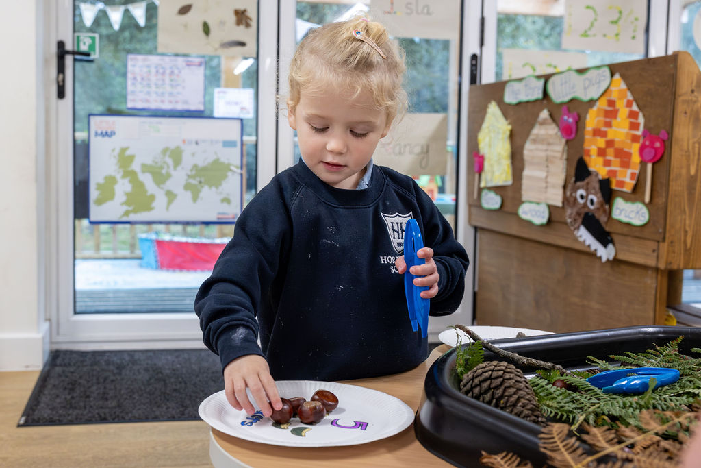 A girl in Horris Hill Nursery uniform plays at the nature table